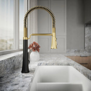 Modern kitchen sink with a gold and black faucet in a well-lit room.