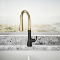 Gold and black kitchen faucet on a marble countertop with a neutral background