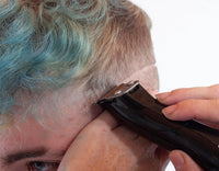 Person with blue and gray hair using a hair trimmer on a white background
