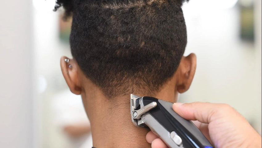Person using a hair trimmer on their head with a blurred background