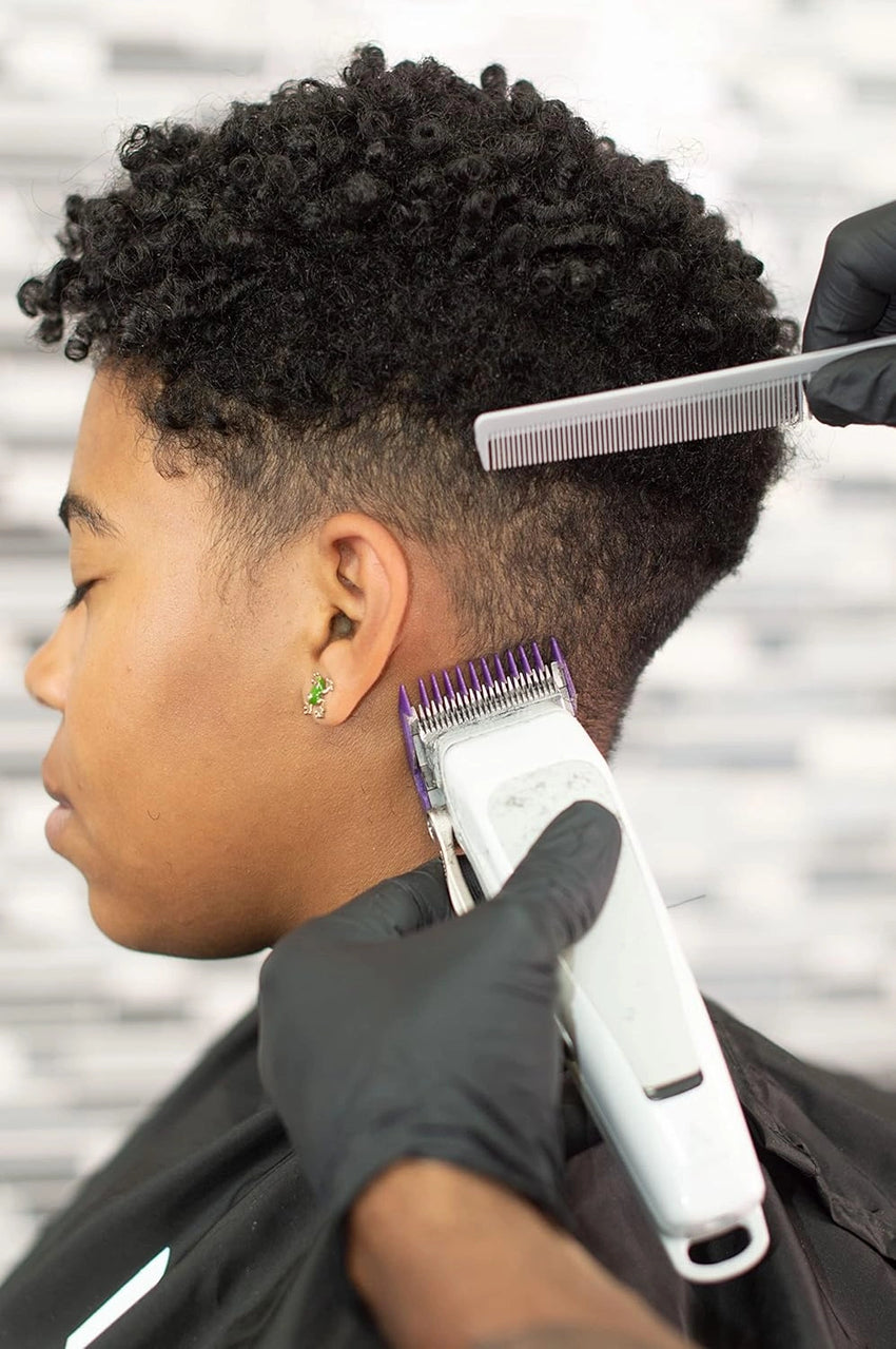 The hairdresser cuts the boy's hair with an Andis clipper and a comb in gloves.