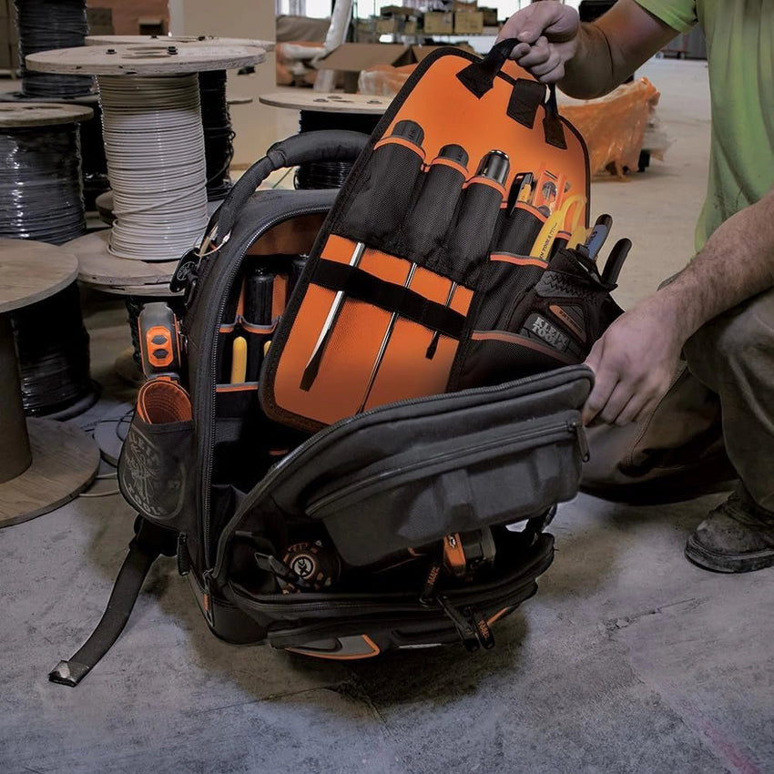 Person organizing tools in a backpack with an orange tool bag in a workshop setting