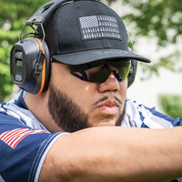 A man wearing a black cap, sunglasses and protective headphones