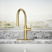 Gold kitchen faucet on a marble countertop with a neutral background