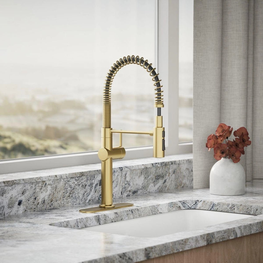 Gold kitchen faucet on a marble countertop with a vase of flowers in the background.