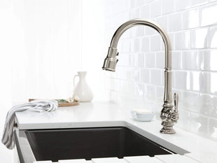 Modern kitchen sink with a silver faucet against a white tiled wall.