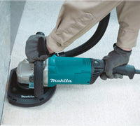 Person using a Makita power sander on a concrete surface